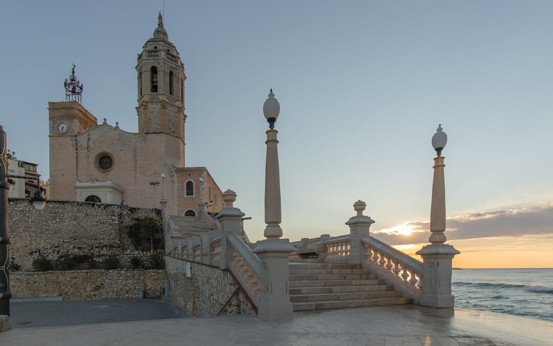 : Sant Bartomeu i Santa Tecla church in Sitges at sunset, the town's iconic landmark for expats seeking natural therapies